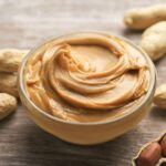 Creamy peanut butter on a knife, ready to be spread on a slice of whole-wheat bread, showcasing a healthy and nutritious snack option