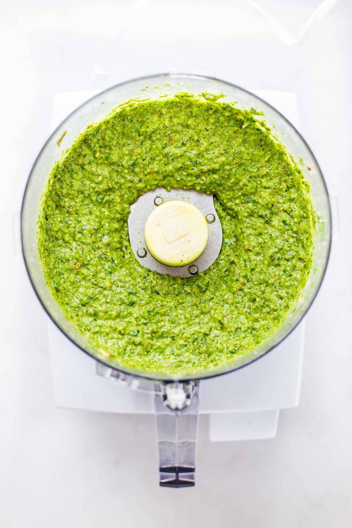 Fresh basil pesto being made in a food processor, highlighting the appliance's ability to create flavorful sauces.