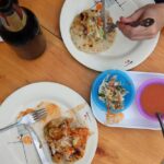 Two pupusas on a wooden table with curtido and salsa