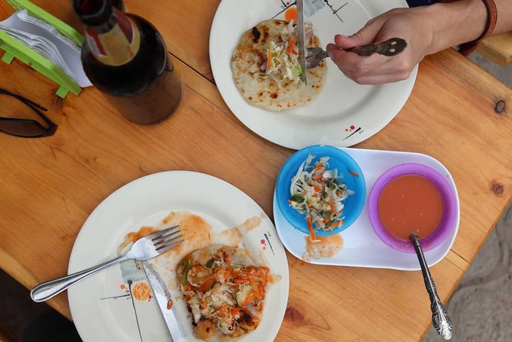 Two pupusas on a wooden table with curtido and salsa