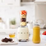 Smeg personal blender in cream on a countertop with a smoothie bottle beside it