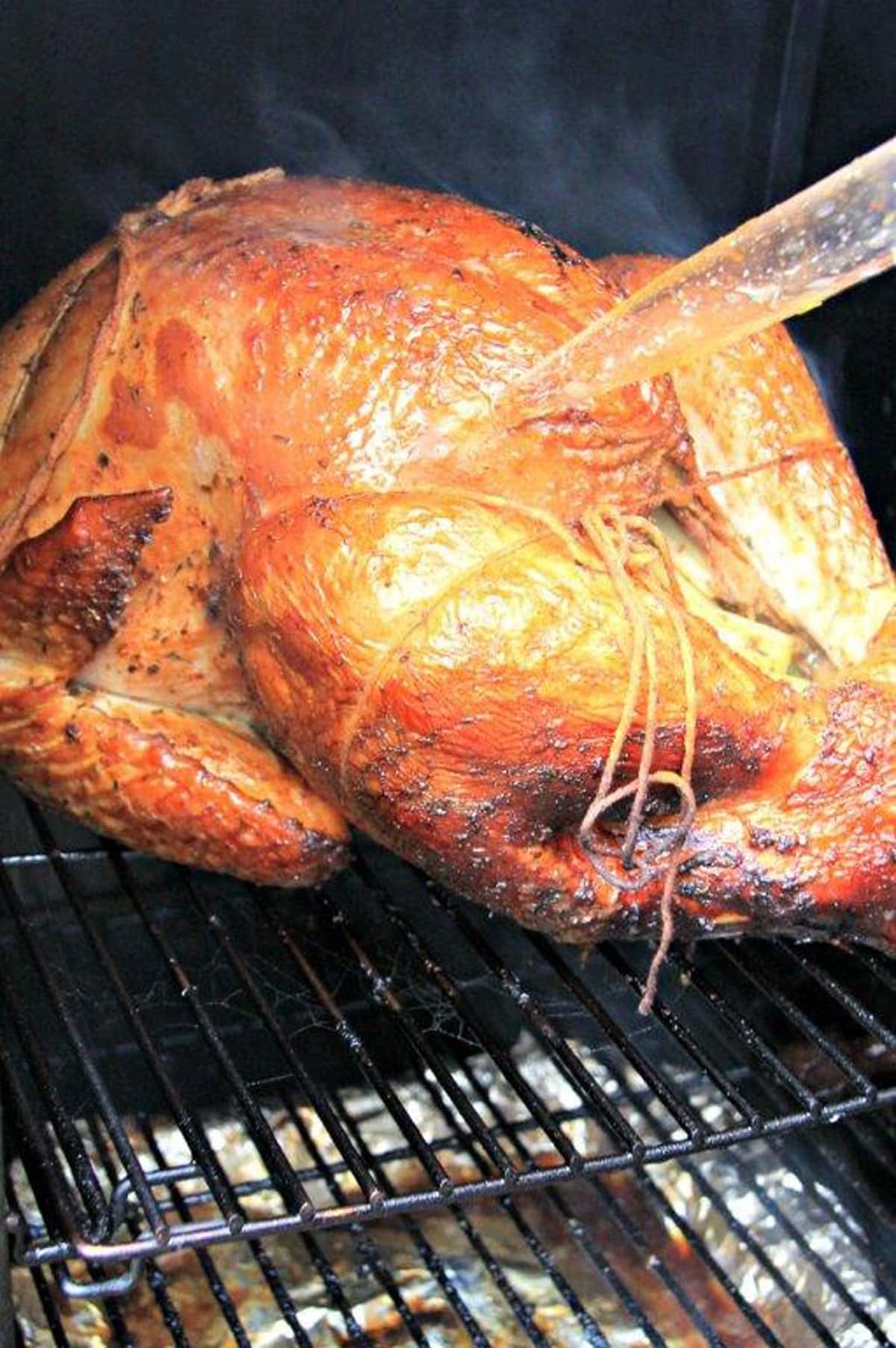 Whole turkey being basted on a smoker.