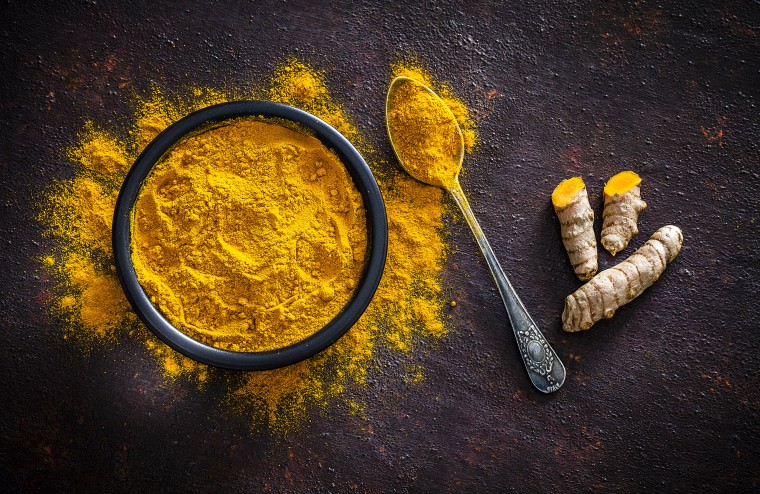 Ground turmeric powder in a bowl next to fresh turmeric root