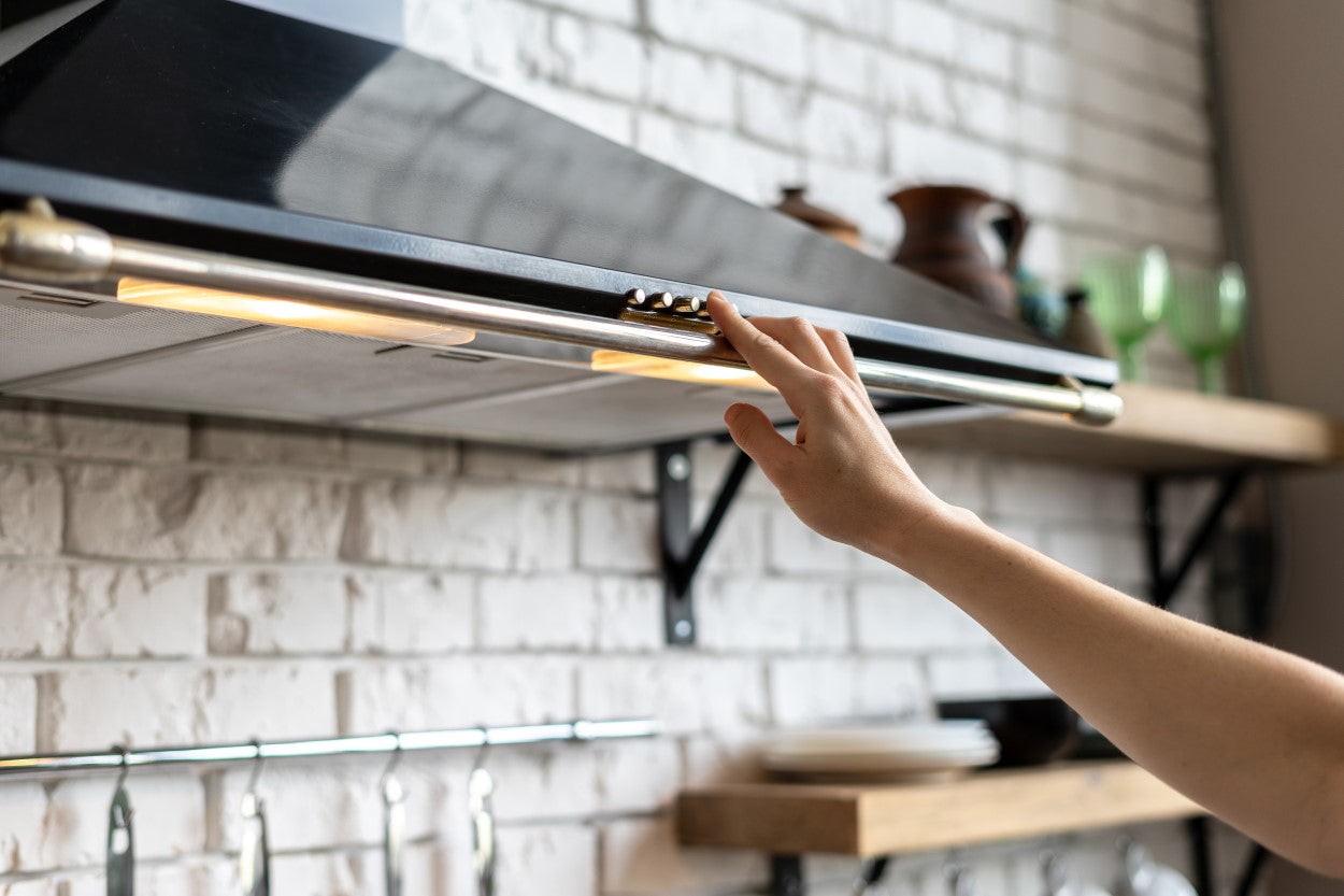 Person turning on range hood to ventilate kitchen