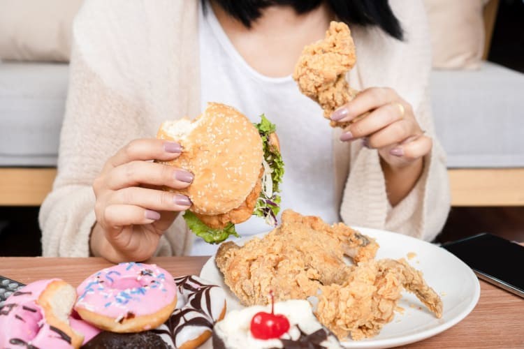 Woman eating fast food burgers, fried chicken, donuts and desserts.