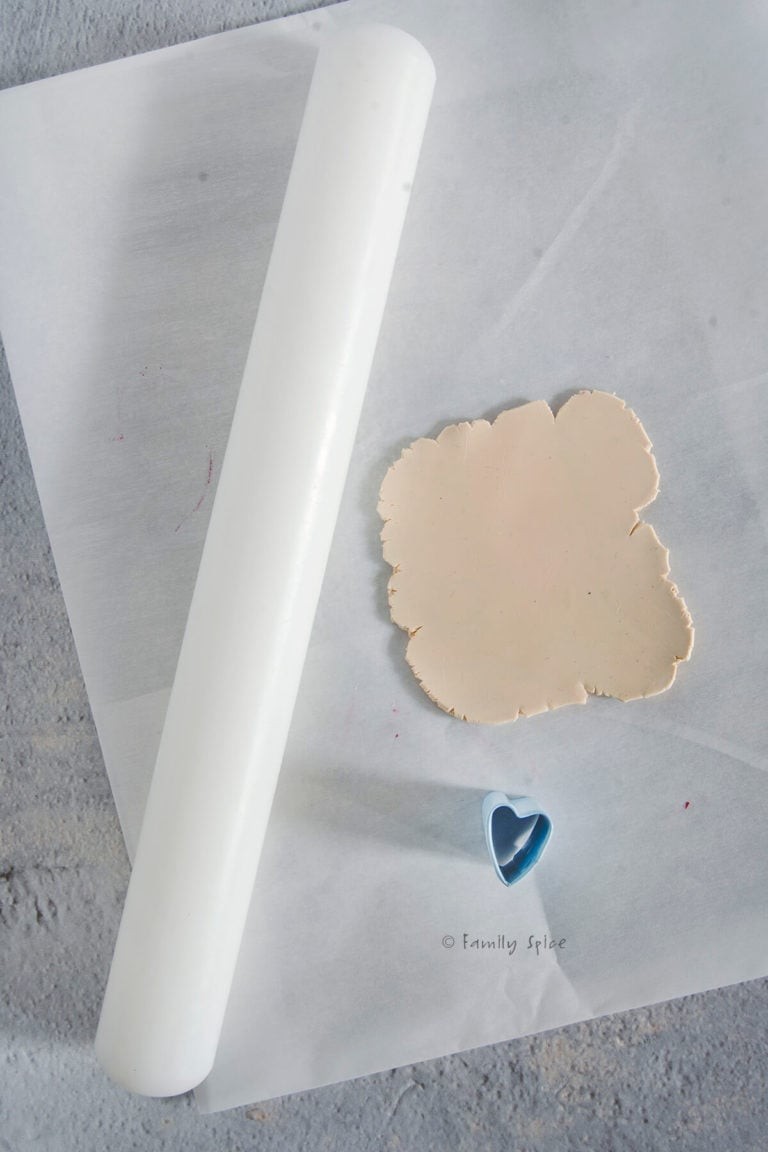 Rolling out beige polymer clay to make miniature heart cookies