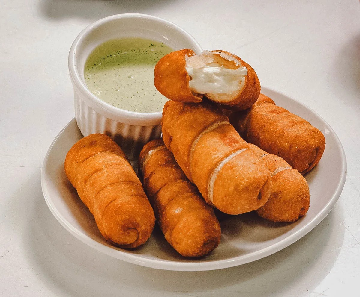 A plate of golden-brown tequeños, served with a dipping sauce
